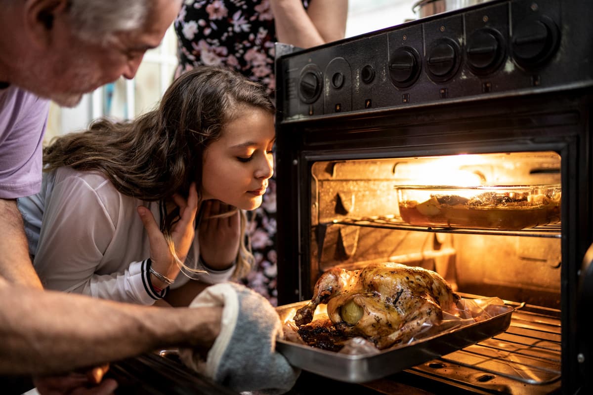 Capa - Ceia de Natal: 10 receitas indispensáveis para o seu cardápio. Receitas de Ceia de Natal: Homem colocando frango no forno , ao lado uma menina