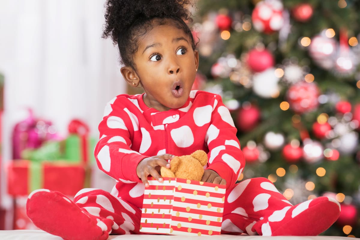 Presentes de Natal: menina negra com cara de surpresa, com a mão em um presente