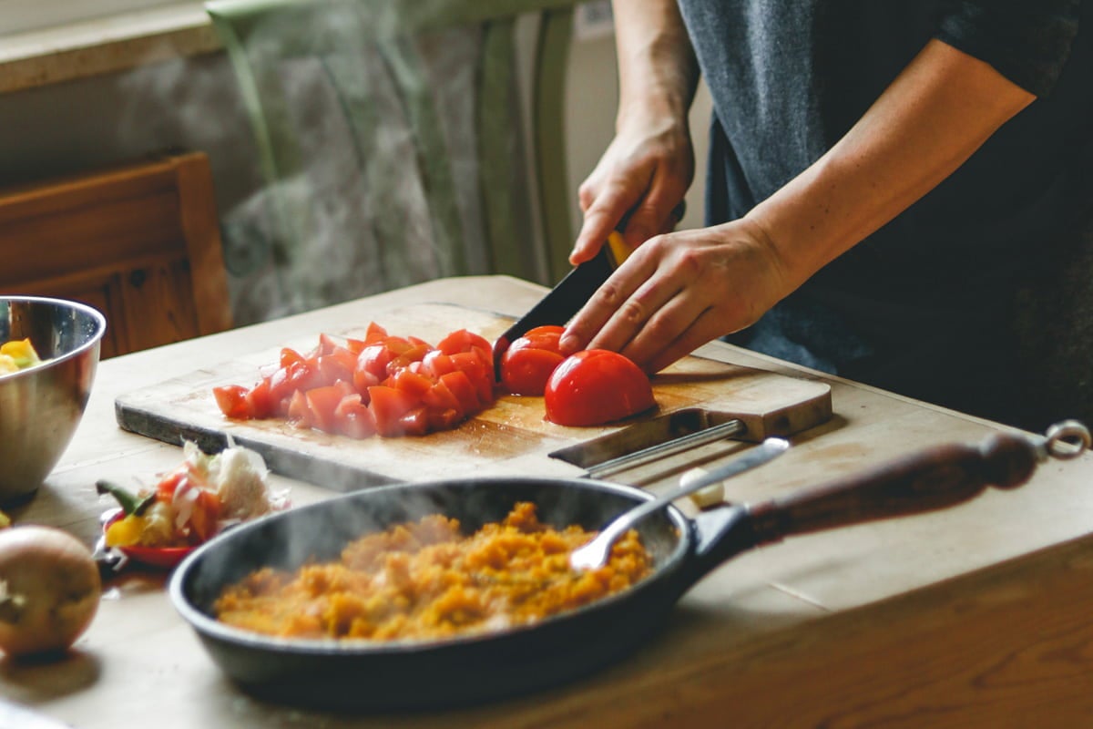Comida italiana: uma pessoa cortando tomate em cima da tábua de madeira