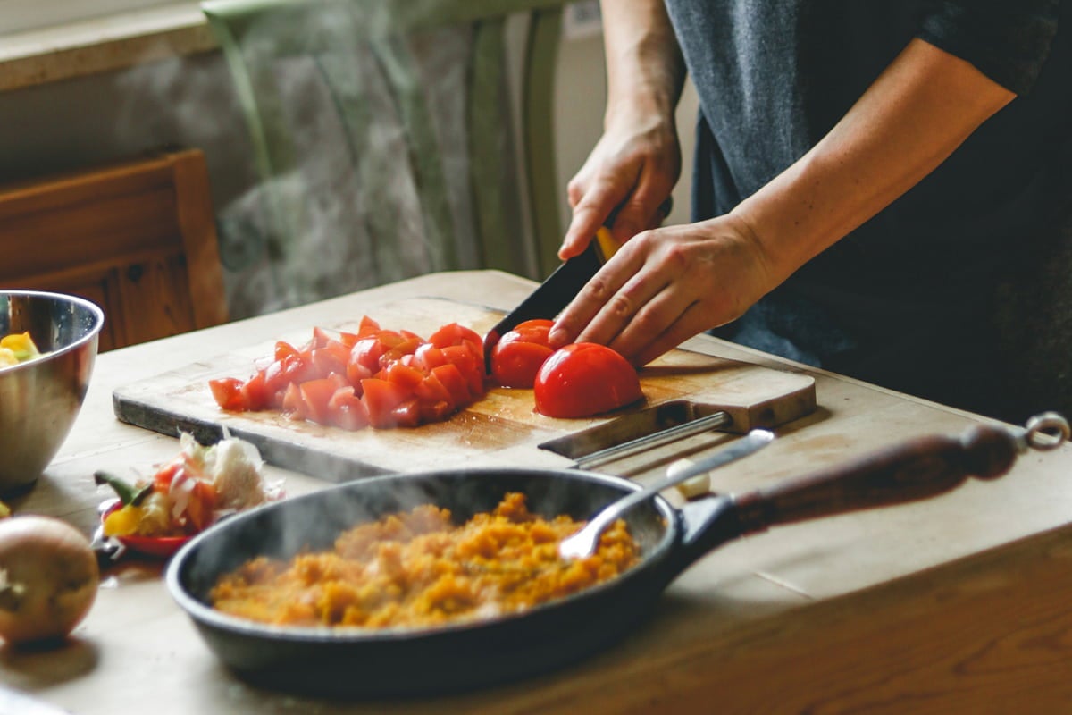 Capa Comida italiana: 15 receitas práticas e deliciosas que vão trazer a Itália para sua casa! Comida italiana: uma pessoa cortando tomate em cima da tábua de madeira