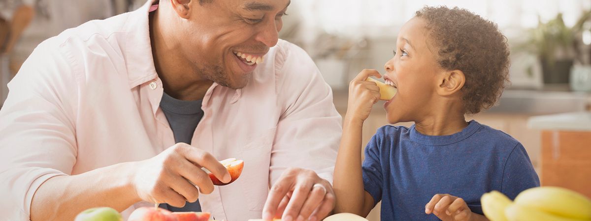 capa Lanche da Tarde: 20 receitas práticas para sair do básico! Lanche da Tarde: Um homem negro com uma maçã na mão e uma criança negra comendo uma maçã