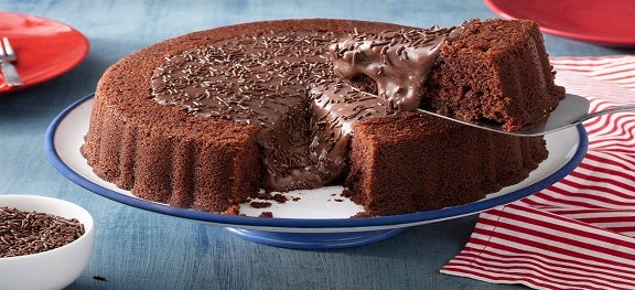 Prato de bolo branco com detalhes azuis. Por cima, um bolo de chocolate coberto com brigadeiro e granulado. Prato de bolo branco com detalhes azuis. Por cima, um bolo de chocolate coberto com brigadeiro e granulado.