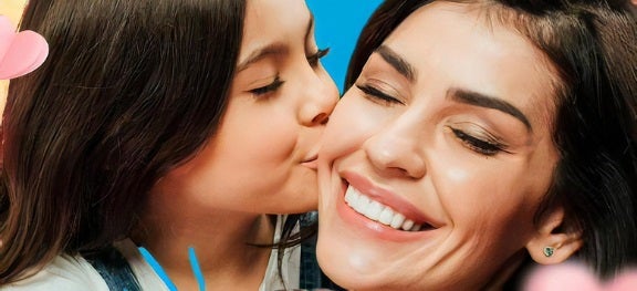 Menina beija a bochecha da mãe, que sorri. As duas estão de olhos fechados. Menina beija a bochecha da mãe, que sorri. As duas estão de olhos fechados.