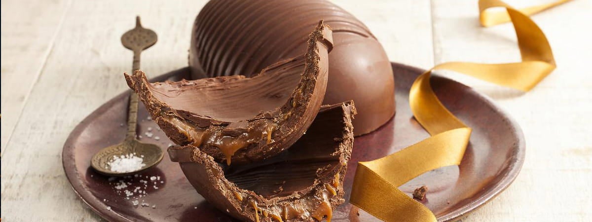 Capa: Receitas de Ovos de Páscoa Receitas de Ovos de Páscoa: Ovo de páscoa de chocolate cortado no meio, em cima de um prato ao lado de uma colher