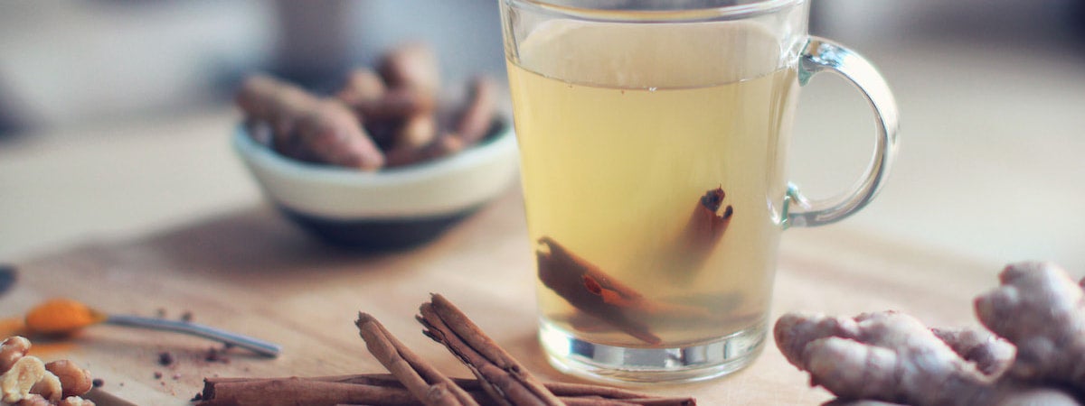 Chá de Gengibre: chá de gengibre em uma xícara, com canela dentro e em volta da xícara, em cima de uma mesa de madeira