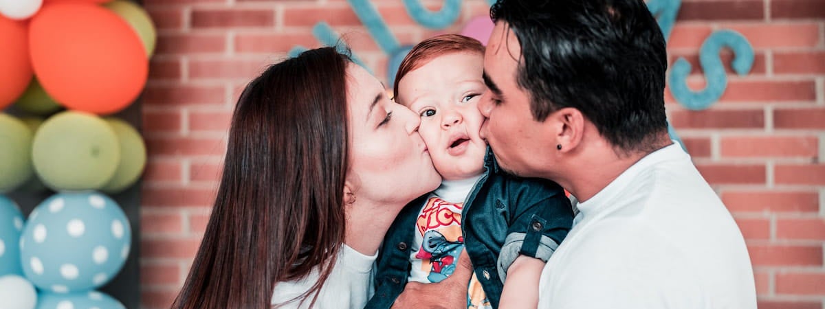 Dia do beijo: Uma mulher á direita e um homem à esquerda, ambos beijando um bebê no meio