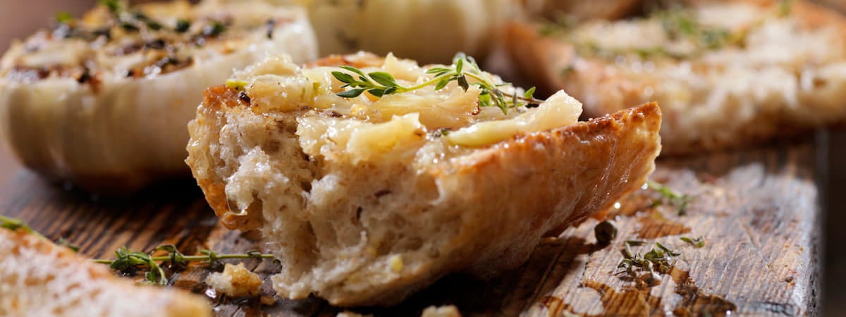 Capa: Pão de Alho Pão de alho caseiro: Pedaço de pão de alho caseiro em cima de uma mesa de madeira