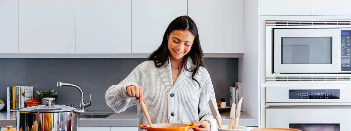 Como economizar gás de cozinha: Mulher sorrindo em uma cozinha com as mãos em uma panela 
