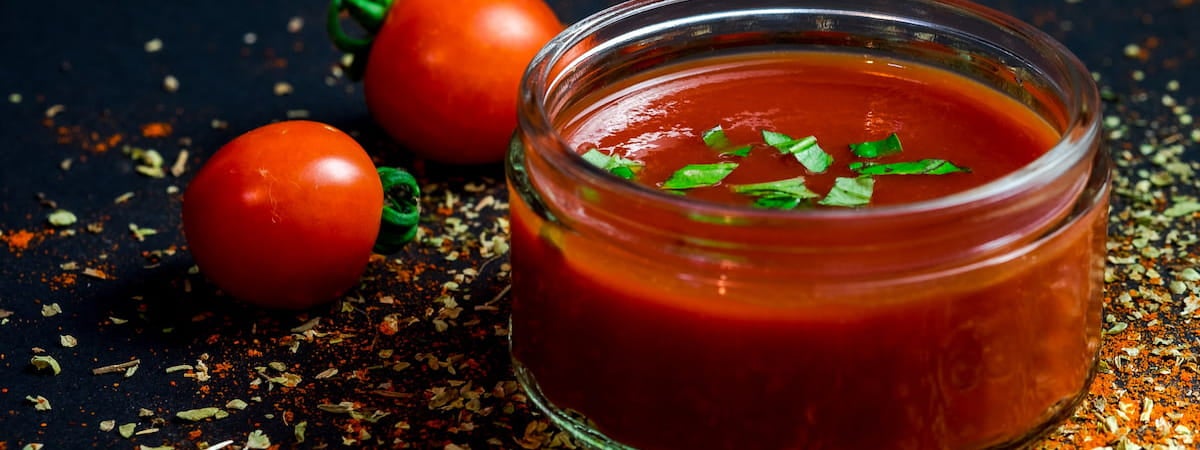 Molho de tomate caseiro: Molho de tomate em um pote de vidro, ao lado de dois tomates