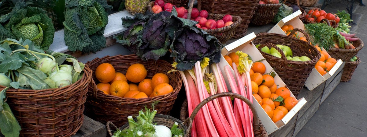 Na foto temos uma bancada de frutas, verduras e legumes típicos do mês de Julho. Frutas de julho, verduras de julho: Várias frutas e verduras em cestas