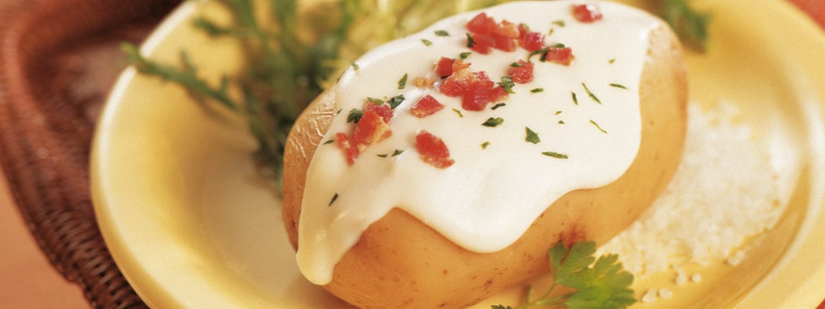 Capa: baked potato Prato com batata recheada e coberta por um molho branco e pedaços de tomate
