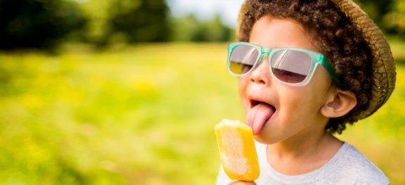 Menino usando óculos de sol e chapéu, tomando picolé em um parque. Menino usando óculos de sol e chapéu, tomando picolé em um parque.
