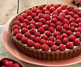 Imagem de uma torta redonda decorada com framboesas sobre um prato