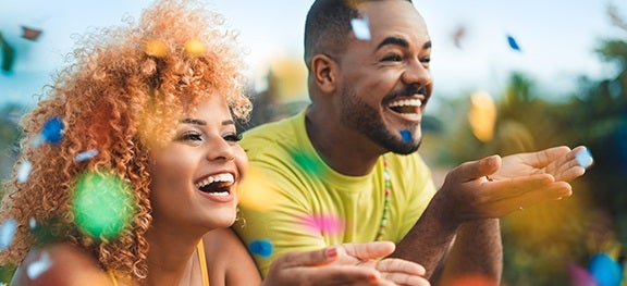 Casal soprando confetes e sorrindo. Eles usam roupas mais vibrantes. Casal soprando confetes e sorrindo. Eles usam roupas mais vibrantes.