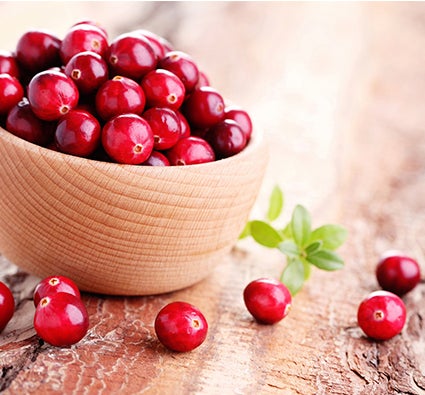 Tigela de madeira com cranberries frescos sobre superfície rústica, com algumas frutas espalhadas ao redor.