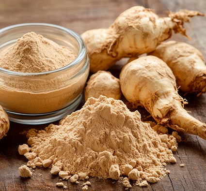 Raízes de maca peruana e pó em recipiente e montinho sobre mesa rústica de madeira.
