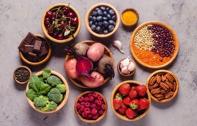 Tigelas com frutas, vegetais, sementes e chocolate amargo, representando alimentos ricos em antioxidantes naturais.