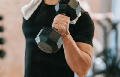 pessoa com blusa preta e uma toalha de rosto em volta do pescoço, segurando um halter com os cotovelos flexionados.