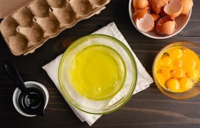 Texto alt: Claras e gemas de ovo separadas em tigelas sobre mesa de madeira, representando a albumina.