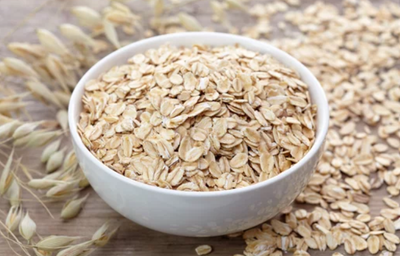 Bowl branco com aveia e grãos de aveia em volta.