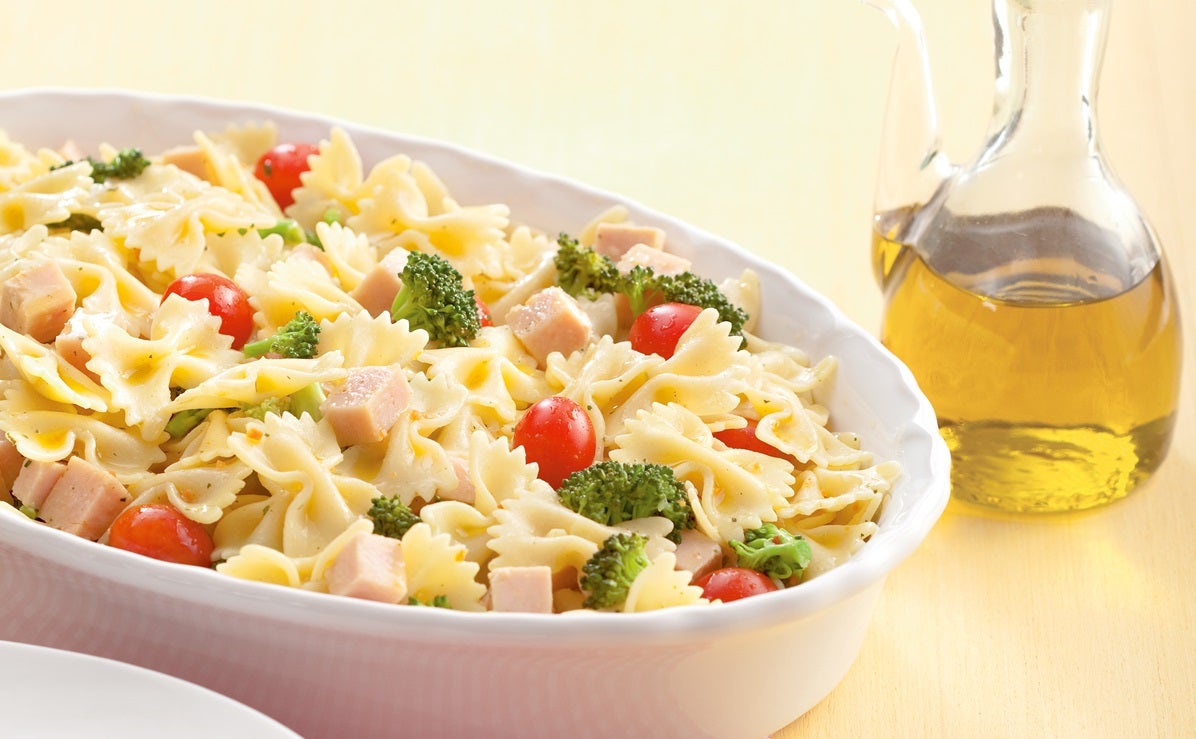 Imagem de uma travessa branca com macarrão gravatinha, peito de peru, brócolis e tomatinhos.