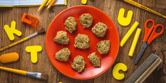Prato vermelho com biscoitinhos redondos, tesouras, letras, pincéis e apontador ao redor.