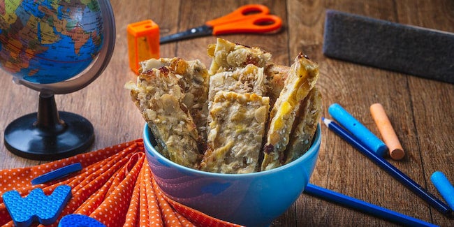Bowl azul com barras de cereais e materiais escolares ambientando.