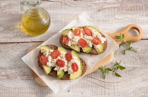 Duas fatias de avocado toast com patê de ricota com tomates sobre uma tábua.