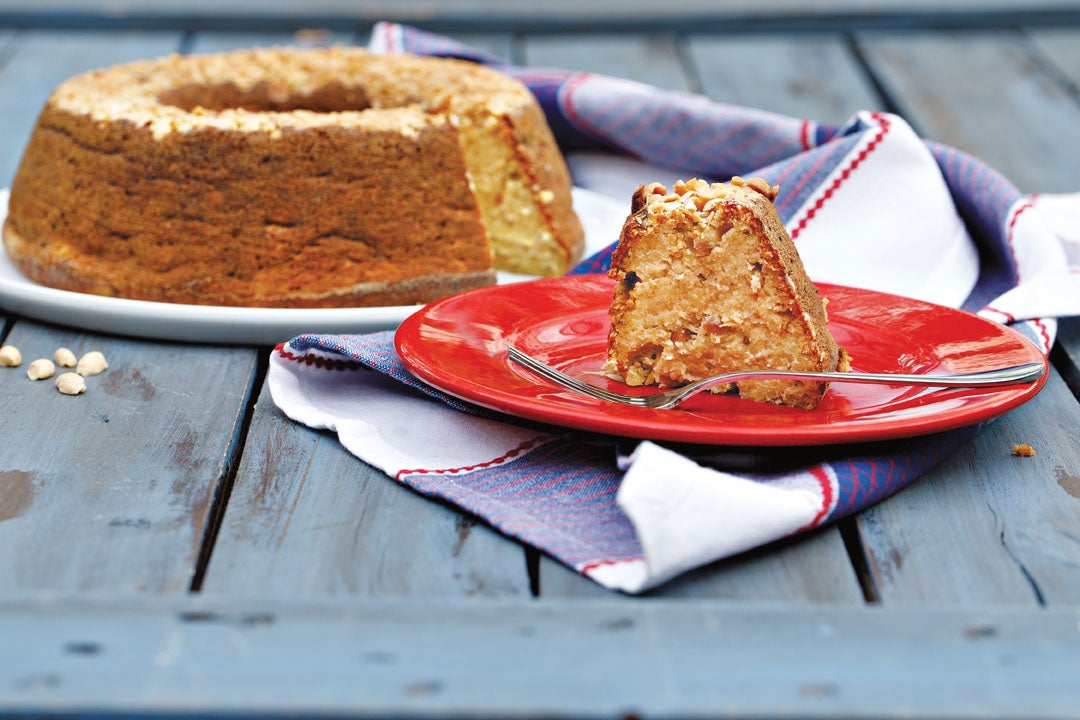 Imagem de um prato vermelho com uma fatia de bolo de batata-doce e amendoim e um prato ao fundo com o bolo restante.