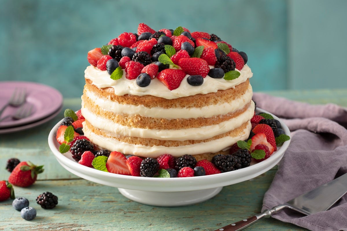 Imagem de um bolo naked cake com camadas de recheio e decorado com morangos e frutas vermelhas no topo.