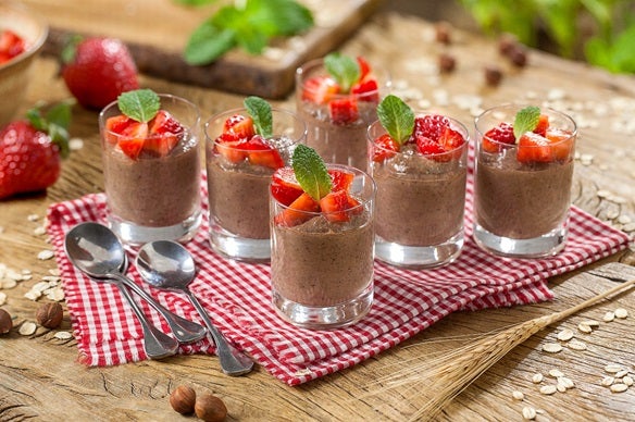 Imagem de copinhos de vidro com creme de avelã e banana com morangos decorando.