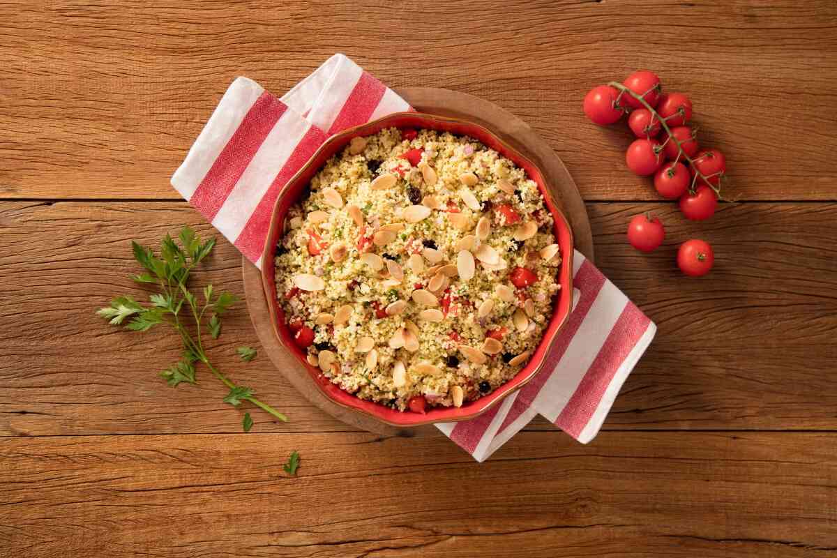 Travessa vermelha com cuscuz marroquino com tomate, uva-passa e amêndoas em lascas.
