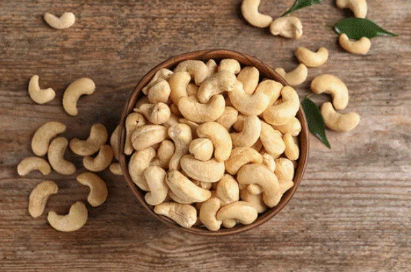 Bowl com castanhas de caju em cima de uma superfície de madeira.