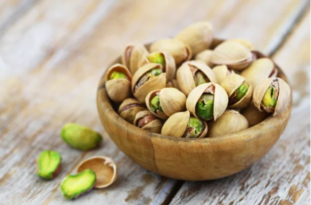Bowl com pistaches em cima de uma superfície de madeira.