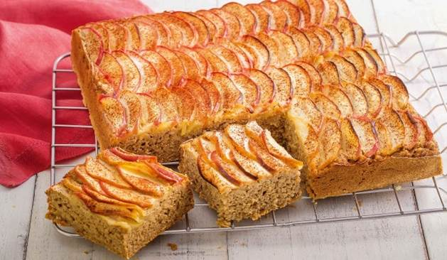 Bolo de maçã com fatias de maçãs decorando sobre uma grade e dois pedações cortados.