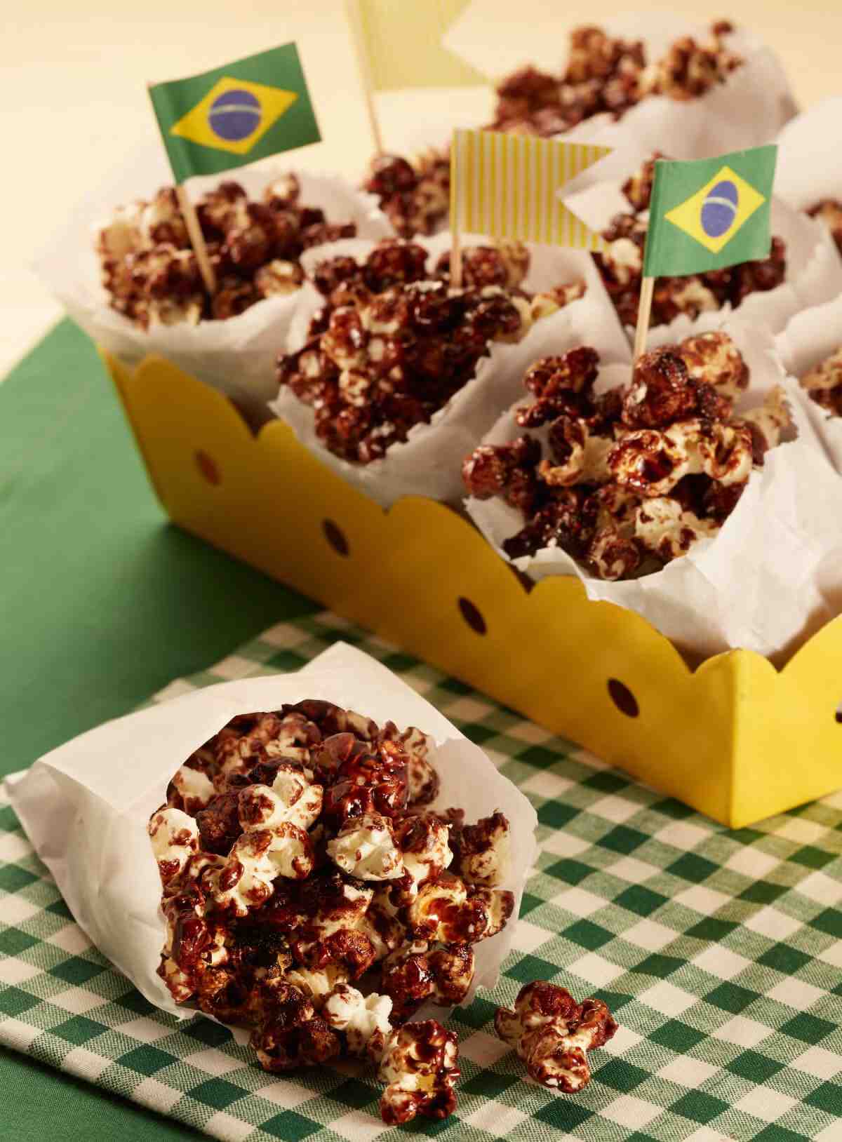 Saquinhos de papel com pipoca doce de chocolate e bandeirinhas do Brasil.
