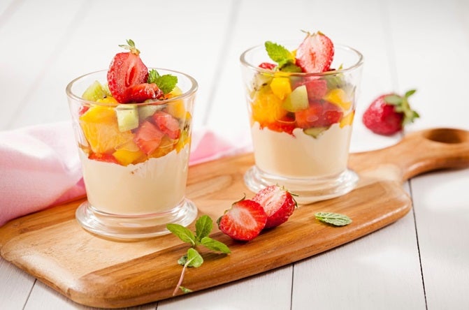 Dois copos de vidro com creme e salada de frutas em cima.