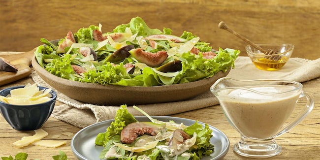 Prato com salada de folhas, figo, mel e queijo parmesão com molho ao lado.