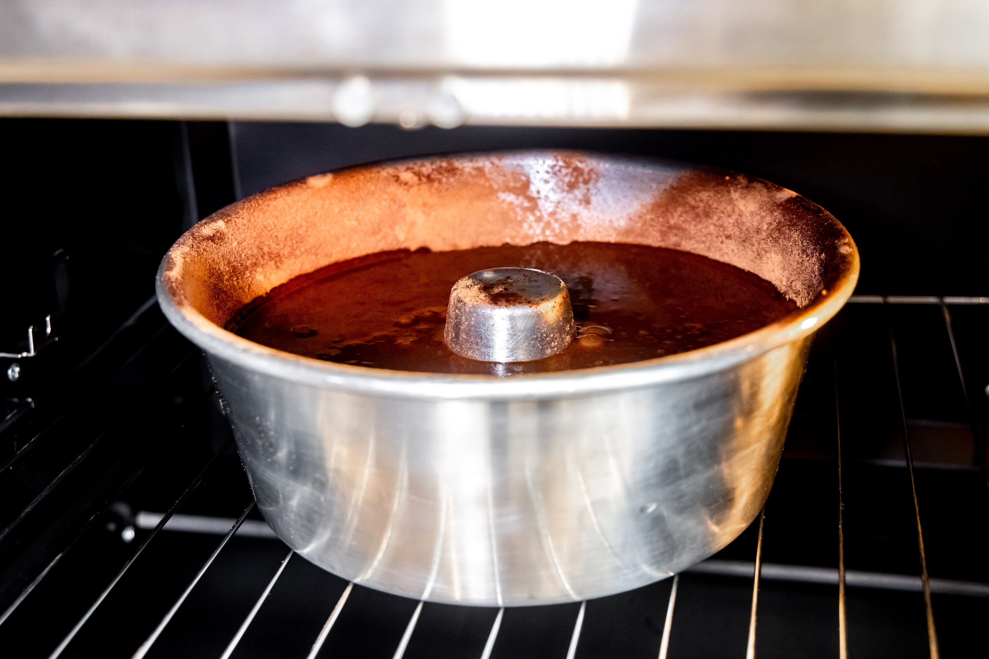 Foto aproximada de uma forma de alumínio de furo central com a massa do bolo dentro. Ela está dentro de um forno.