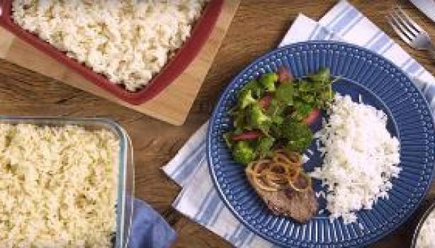 Como Fazer Arroz Soltinho Tela de vídeo mostra uma mesa com uma travessa de arroz branco, uma de arroz integral e um prato com arroz, bife e salada