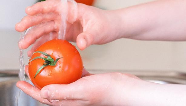 Como higienizar frutas, verduras e alimentos: uma pessoa lavando um tomate na pia