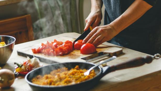 Comida italiana: uma pessoa cortando tomate em cima da tábua de madeira