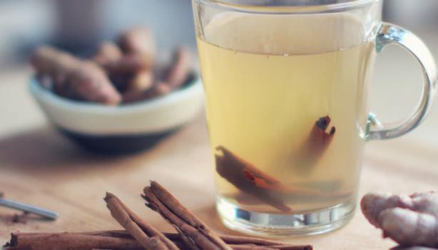 Chá de Gengibre: chá de gengibre em uma xícara, com canela dentro e em volta da xícara, em cima de uma mesa de madeira