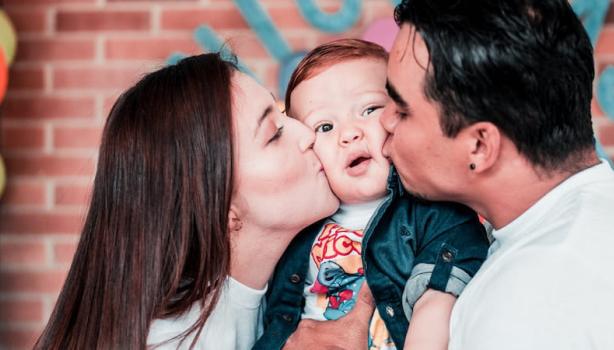 Dia do beijo: Uma mulher á direita e um homem à esquerda, ambos beijando um bebê no meio
