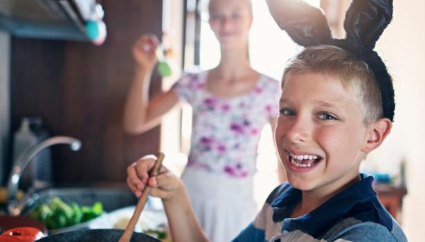 Sexta-Feira Santa: Menino com tiara de coelho sorrindo enquanto segura uma colher ao lado da mãe na cozinha