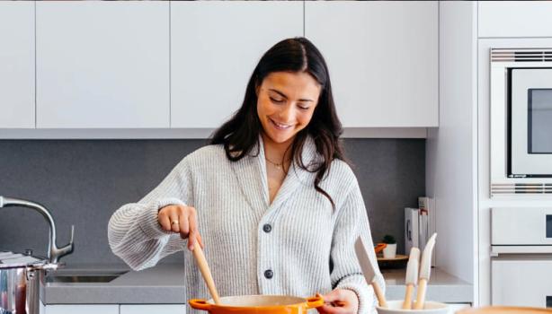 Como economizar gás de cozinha: Mulher sorrindo em uma cozinha com as mãos em uma panela 