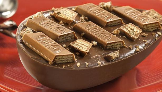 Ovo de colher: Ovo de páscoa com pedaços de chocolate KitKat em cima, em um prato ao lado de uma colher