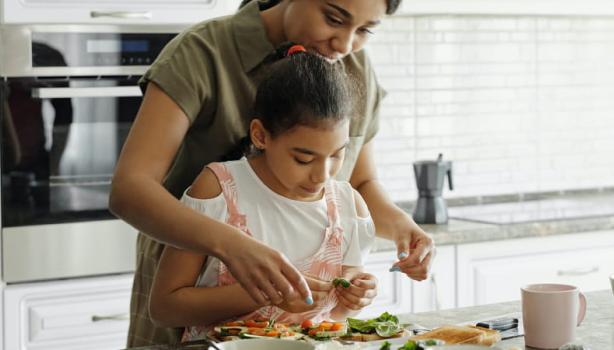 Almoço de Dia das Mães: Mulher negra adulta na cozinha ajudando criança negra a cozinhar