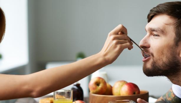 Café da Manhã Romântico: Mulher à esquerda colocando uma colher com comida na boca de um homem à direita