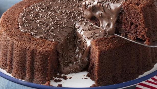 Receitas com Nescau:Bolo de chocolate com cobertura de chocolate, à direita uma pessoa retirando um pedaço do bolo